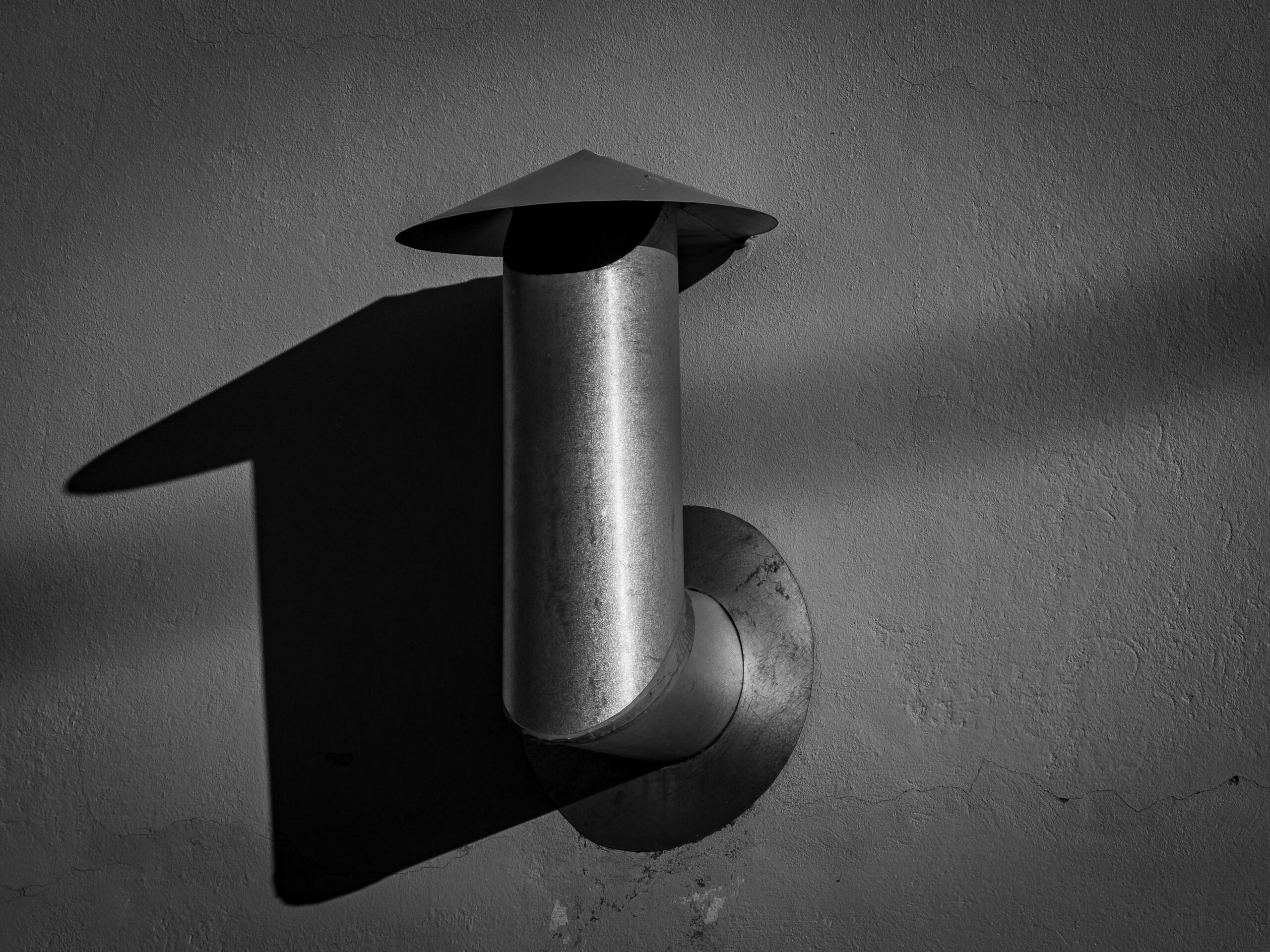 Black and white image of a metal pipe creating a striking shadow on a wall.
